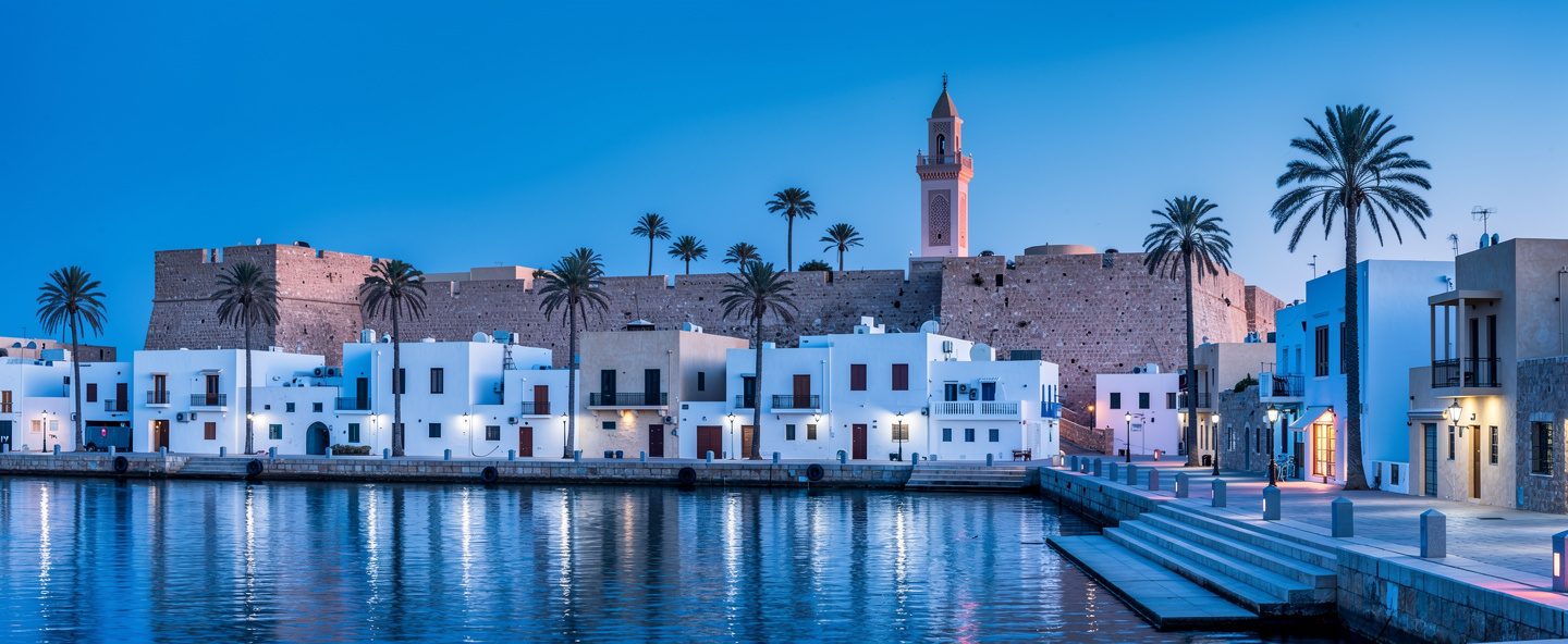 مدينة ساحلية متوسطية عند الغسق بأسوارها القديمة ومئذنتها ونخيلها